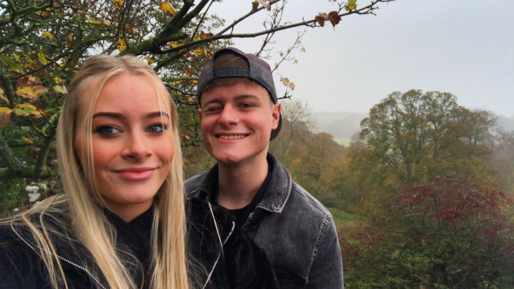 Picture of Matt with a person with long blonde hair, Matt is wearing a cap backwards, both are wearing black clothing. 