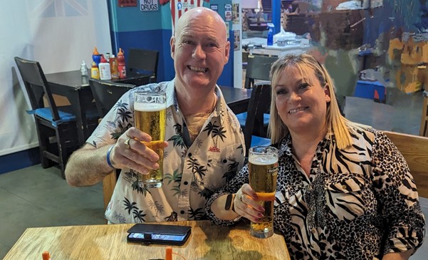 Dave is pictured with his wife in a bar on holiday with a pint of beer in his hand.