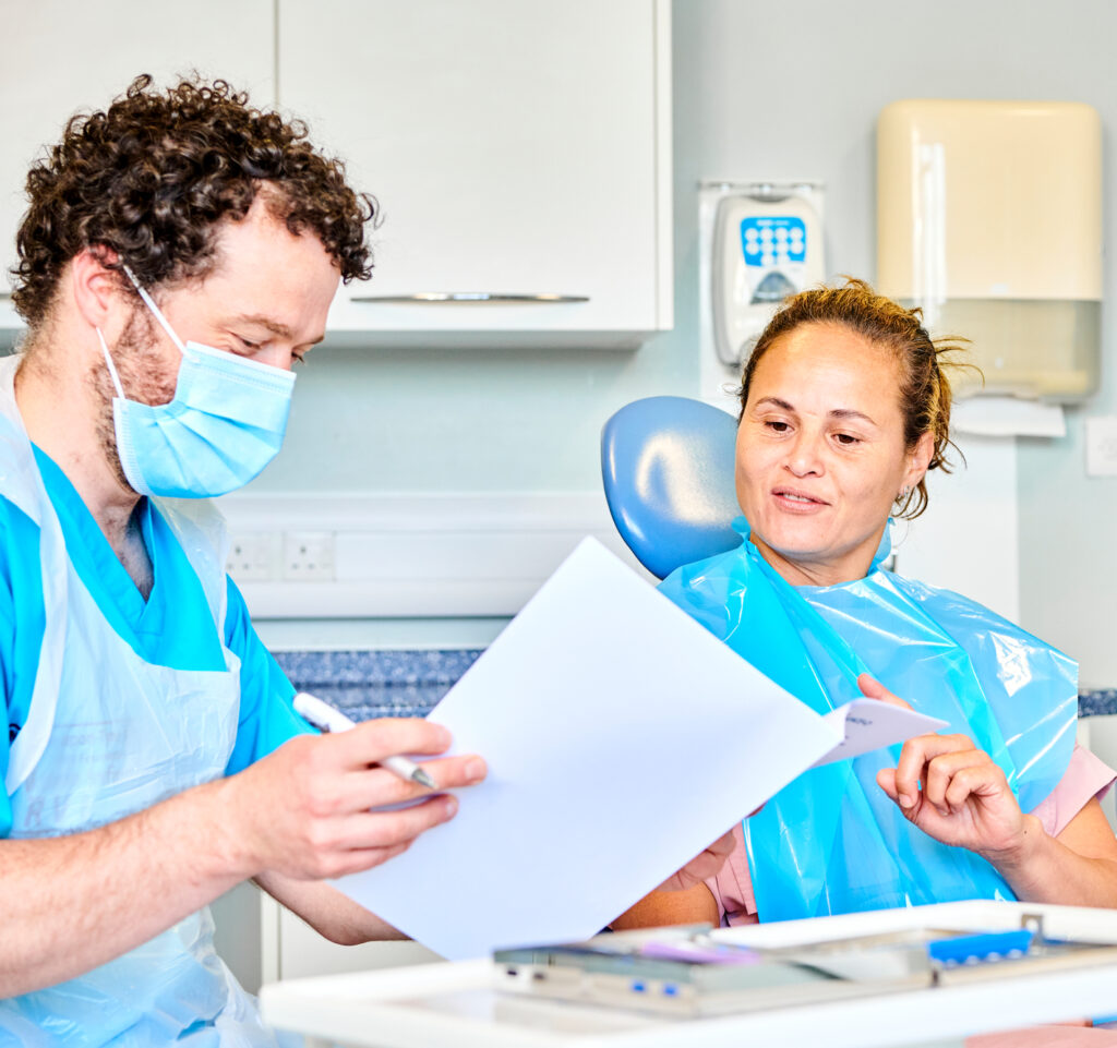 A dentist sits with a patient showing them some information on a piece of paper