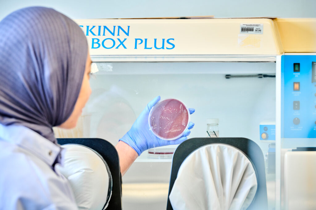 A scientist in a lab holds a petri dish in front of her