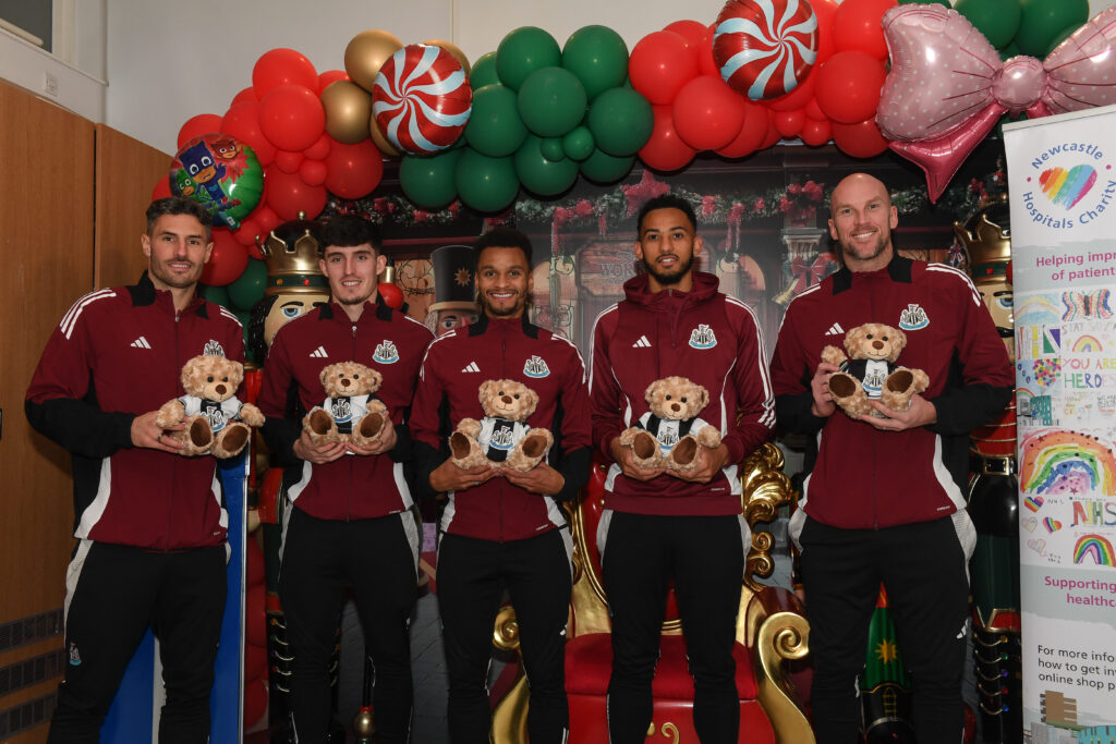 Five Newcastle United players stand with teddy bears under an arch of balloons. The teddies are wearing black and white t-shirts that were made from previous kits,