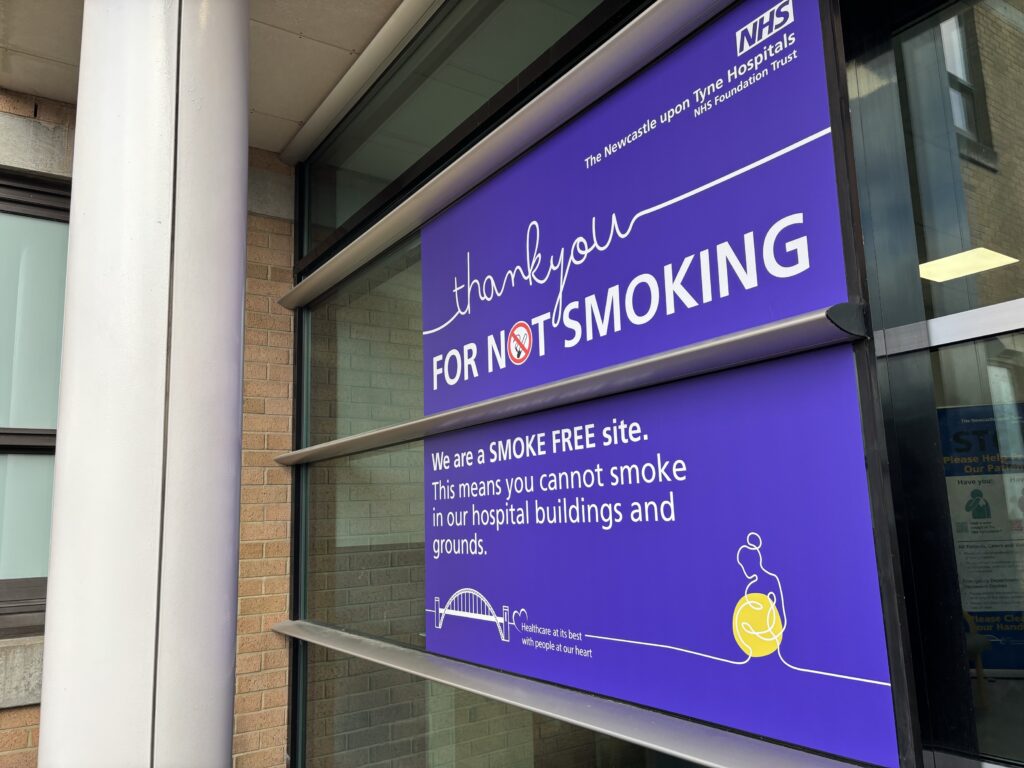 Purple signage on the window at the RVI. It has the text "Thank you for not smoking. We are a smoke free site. This means you cannot smoke in our hospital buildings and grounds.