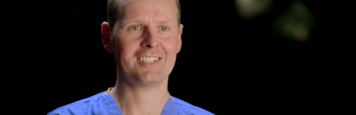 Picture of Tom Oliphant in blue scrubs smiling.