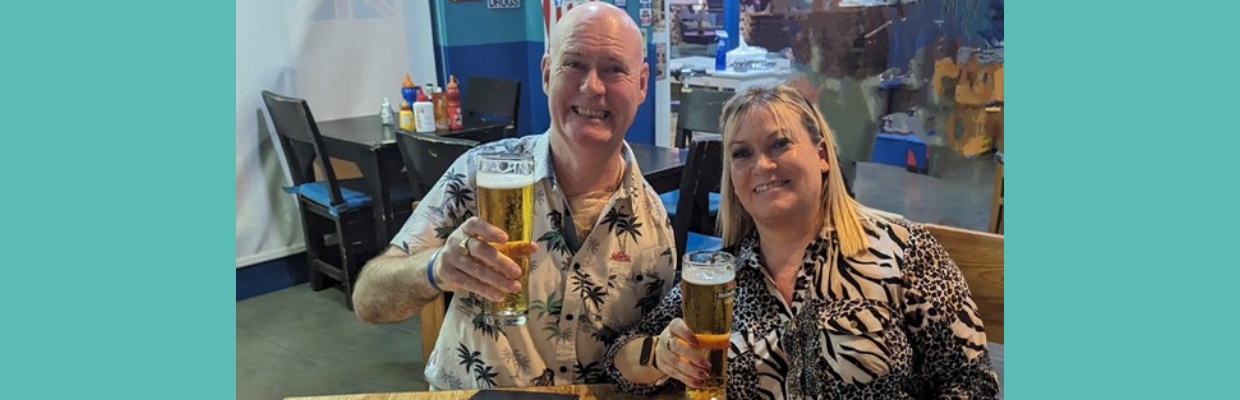 Dave is pictured with his wife holding a pint of beer in a bar abroad.