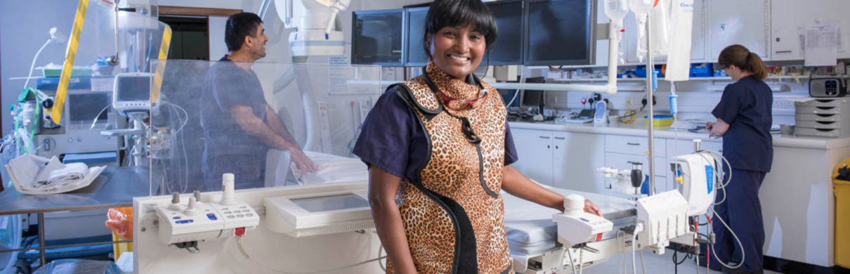 Prof Vijay Kunadian stands in a surgical theatre with two colleagues dressed in scrubs in the background.