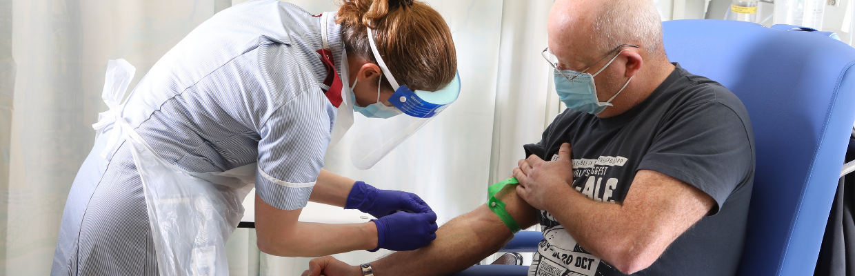 A nurse prepares to draw blood from the arm of a patient sat in a blue chair